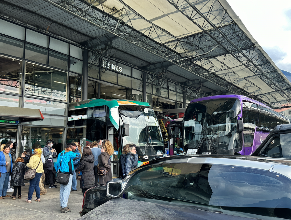 Busy bus terminal exterior showing passengers and buses ready for travel.