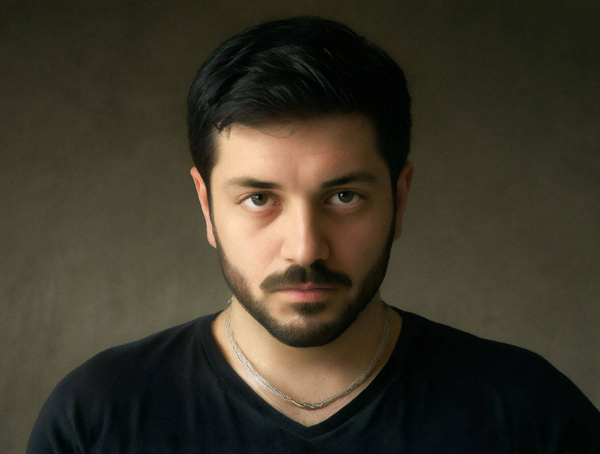 Retrato íntimo de un hombre con barba corta y collar de plata bajo luz suave, transmitiendo una sensación reflexiva y melancólica.