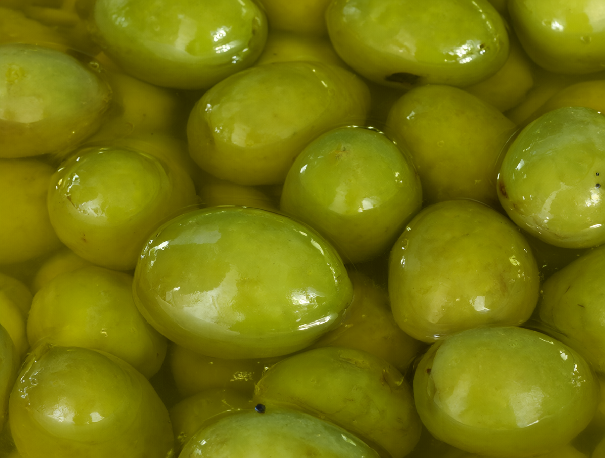 Close-up view of fresh green olives submerged in clear, golden olive oil, capturing their smooth texture and vibrant colors.