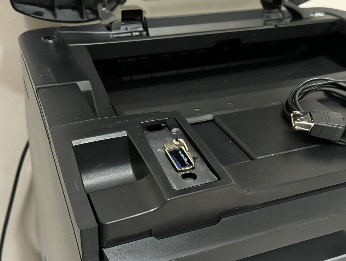 Vista detallada de una impresora con su puerto de conexión USB-B visible junto a un cable específico para impresoras.