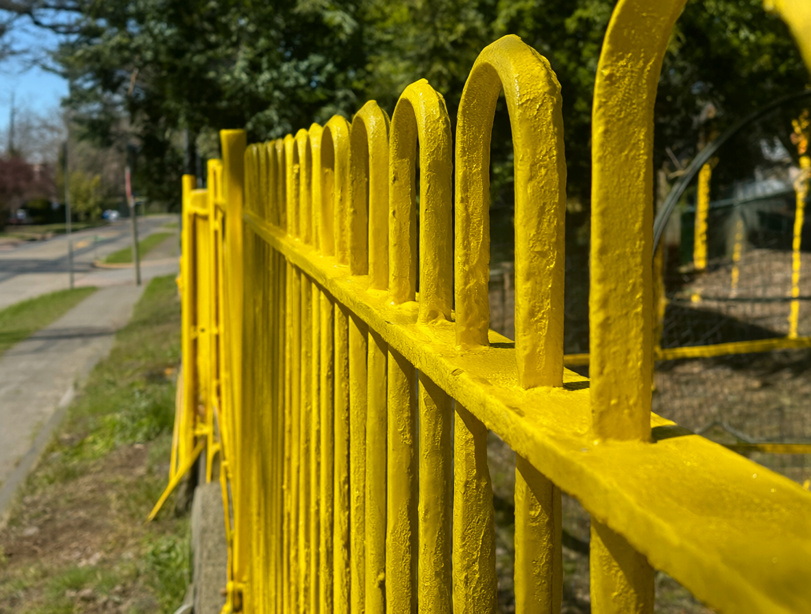Vista cercana de un cerco metálico amarillo recién pintado bajo la luz del sol.