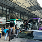 Busy bus terminal exterior showing passengers and buses ready for travel.