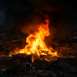 Vista aérea dramática de un barrio residencial envuelto en llamas y humo negro, con bomberos luchando contra el fuego infernal.