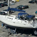 Un velero blanco llamado BATIDA estacionado en un puerto con coches al fondo.