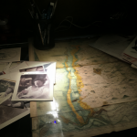 Foto de un escritorio con una foto de Felipe Camiroaga, mapas y documentos bajo luz dramática.
