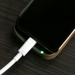 Smartphone enchufado en una mesa oscura, pantalla negra mientras se carga la batería para luego encenderse.