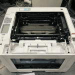 Impresora láser blanca Canon LBP6030W en un entorno de oficina, con el panel abierto revelando su interior.