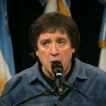 Retrato de Javier Milei hablando en un podio con banderas argentinas