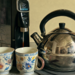 Imagen de un dispensador de agua y una tetera junto a tazas para comparar su uso