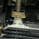 Close-up view of an open toner cartridge inside a printer, showing the white silica powder being distributed by a roller brush.