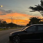 Vista de un estacionamiento vacío al atardecer con un coche detenido en la penumbra.