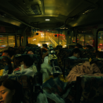 Interior de un autobús lleno de pasajeros durmiendo bajo la luz nocturna.
