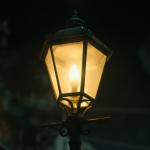 A close-up view of a bright vintage-style streetlamp standing alone in the poster for The Amazing Digital Circus, with dark shadows emphasizing its isolation.