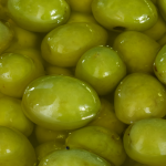 Close-up view of fresh green olives submerged in clear, golden olive oil, capturing their smooth texture and vibrant colors.