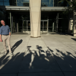 A man standing in front of a courthouse with a shadowy silhouette of a crowd behind him representing public outrage.
