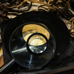 Disco de vinilo de Prince con una lupa encima, sobre un escritorio con cintas de estudio.