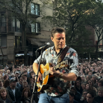 Foto de Kevin Johansen tocando la guitarra en vivo frente a una audiencia.