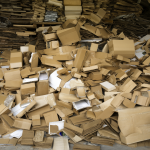 Varias cajas de cartón apiladas en un almacén con materias primas alrededor, representando el olor característico de los envases.