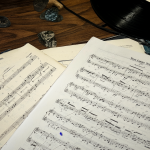 Vintage sheet music for Dire Straits songs displayed on a wooden desk, surrounded by worn guitar picks and vinyl records.