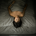A top-down view of an inverted person lying on a bed, head near the foot and feet near the headboard.
