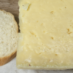 A close-up image showing a block of cheese and a slice of bread together.