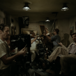Vista del set de filmación con técnicos moviendo muebles alrededor de una cámara fija en los años 40.