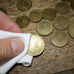 Vista cercana de monedas de 10 pesos chilenas sobre una mesa de madera rústica, siendo limpiadas suavemente con un paño de microfibra.