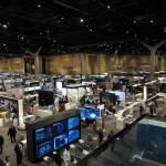 Vista panorámica de un evento tecnológico masivo con stands y pantallas modernas.
