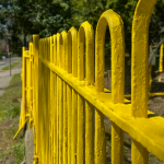 Vista cercana de un cerco metálico amarillo recién pintado bajo la luz del sol.
