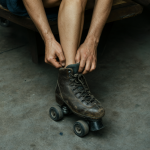 Vista cenital de una persona sentada en un banco, colocándose un rollerskate. Se enfatiza la textura de la piel y el cuero gastado del calzado.